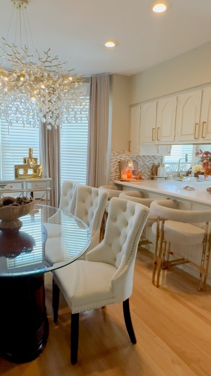 Cream kitchen cabinets and a dining area with white tufted chairs and crystal chandelier.