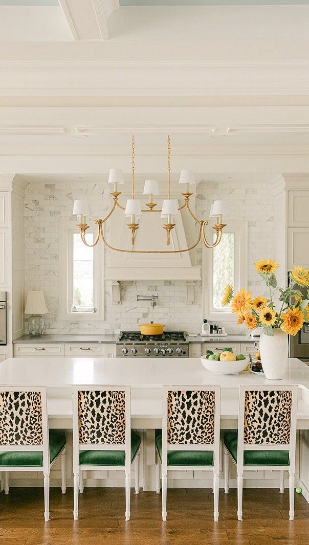 White kitchen with marble countertops, gold chandelier, and leopard print bar stools.