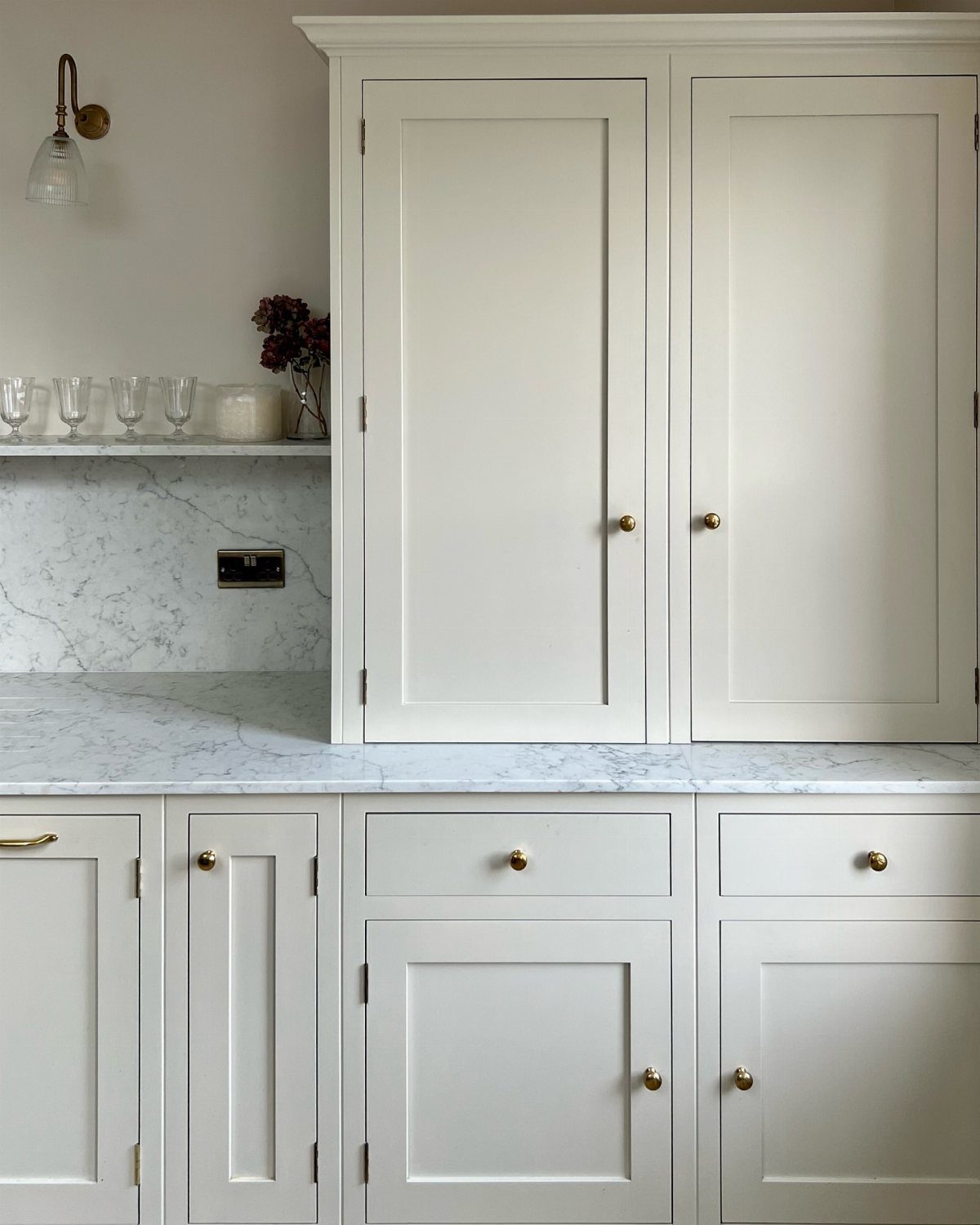 Cream shaker kitchen cabinets with gold hardware and white marble countertops.